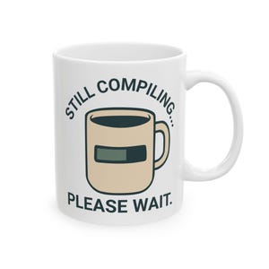 May include: White ceramic mug with the text "STILL COMPILING... PLEASE WAIT." The mug features a graphic of a coffee cup with a progress bar, suggesting a humorous tech or programming theme. The mug has a curved handle.