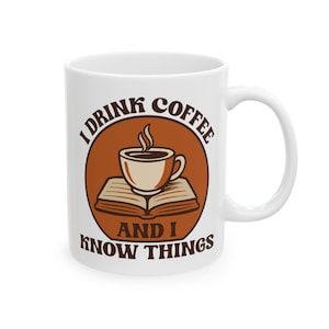 May include: White ceramic coffee mug with a brown graphic. The graphic features a coffee cup above an open book, inside a brown circle. Text reads "I DRINK COFFEE AND I KNOW THINGS."
