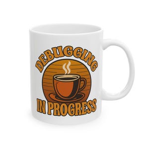 Puede incluir: Taza de café de cerámica blanca con las palabras "DEBUGGING IN PROGRESS" en letras naranjas. La taza presenta un gráfico de una taza de café con vapor ascendente, sobre un diseño de sol en tonos marrones y naranjas.