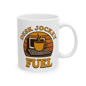 Puede incluir: Taza de cerámica blanca con un diseño retro. La taza presenta un gráfico de una computadora y una taza de café con vapor, sobre un fondo de puesta de sol. Las palabras "DESK JOCKEY FUEL" están impresas en naranja.