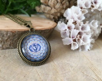 May include: A blue and gold chakra pendant necklace with a bronze chain and a round glass cabochon featuring a mandala design and the symbol for the third eye chakra.
