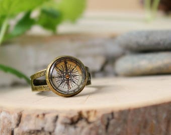May include: A brass ring with a compass design. The compass face is white with black markings and a gold needle. The ring is on a wooden surface.