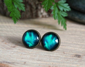 May include: A pair of stud earrings with a dark blue and green galaxy design. The earrings are set in a bronze-colored metal.