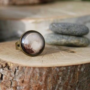May include: A bronze ring featuring a round, white and brown glass cameo. The cameo has a swirling pattern reminiscent of a galaxy.