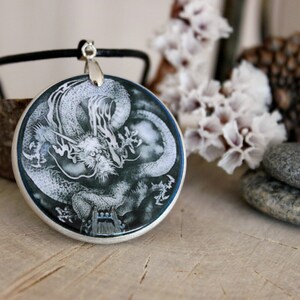May include: A silver pendant necklace with a round, blue and white resin cameo featuring a detailed illustration of a dragon.