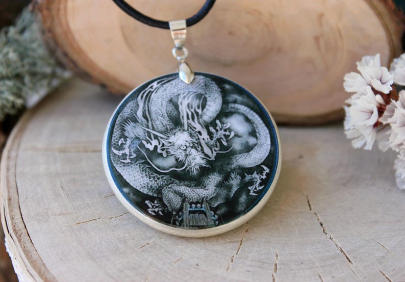 May include: A silver pendant necklace with a black cord. The pendant is a round, white and black cameo featuring a detailed carving of a dragon.