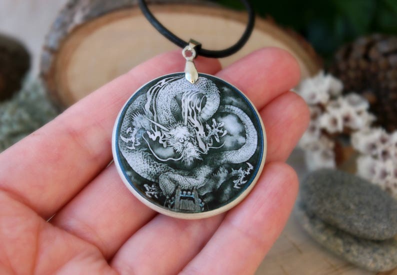 May include: A silver pendant necklace with a black cord. The pendant is a round, white and black dragon design on a dark green background.