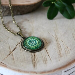May include: A green and gold necklace with a round pendant featuring a green and gold mandala design. The pendant is on a brown chain.