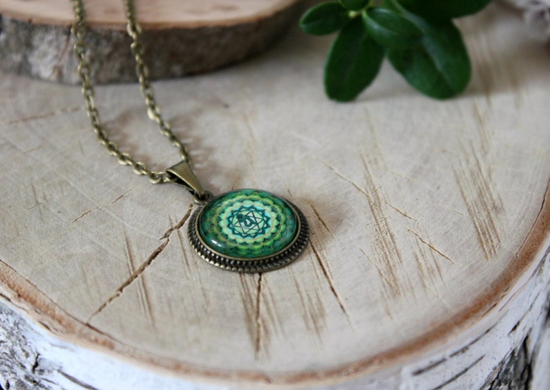 May include: A green and gold necklace with a round pendant featuring a green and gold mandala design. The pendant is on a brown chain.