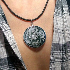 May include: A silver necklace with a black cord and a round pendant featuring a black and white image of a dragon.