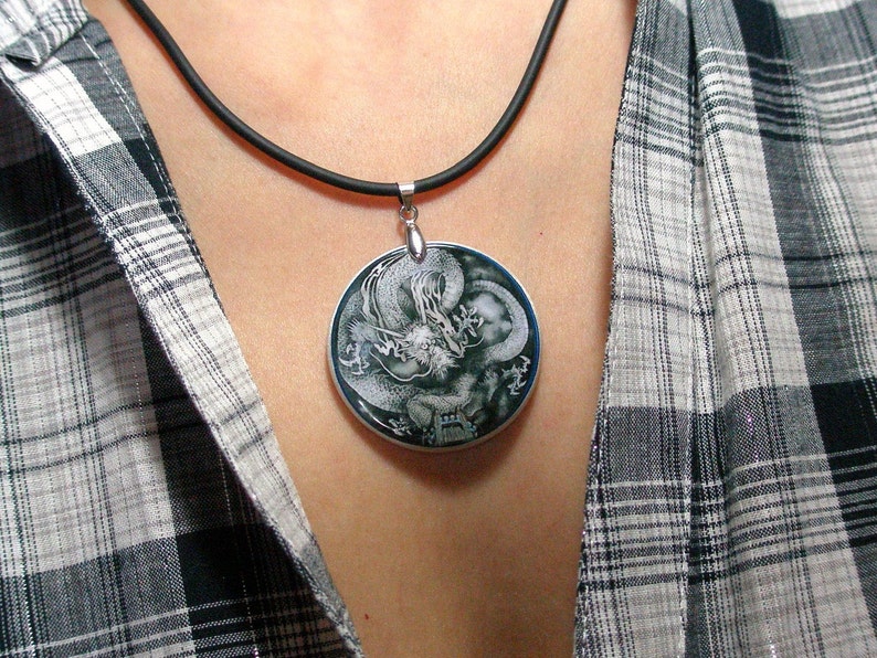 May include: A silver necklace with a black cord and a round pendant featuring a black and white image of a dragon.