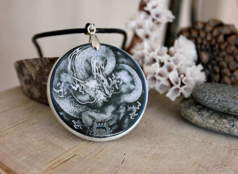May include: A silver pendant necklace with a round, blue and white resin cameo featuring a detailed illustration of a dragon.