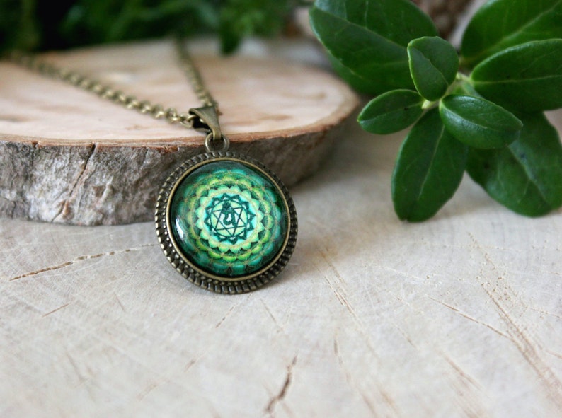 May include: A green and gold necklace with a round pendant featuring a green and gold mandala design. The pendant is surrounded by a bronze-colored frame.