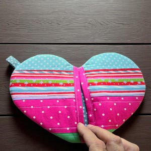 May include: Heart-shaped quilted potholder with a loop for hanging. The potholder features a vibrant design with pink, blue, green, and red stripes and polka dots. The potholder is made of fabric and has a stitched design.