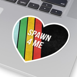 May include: A heart-shaped sticker with the text "SPAWN 4 ME" in white. The sticker features vertical stripes in green, light blue, yellow, and red, with a black textured area. The sticker is placed on a laptop.
