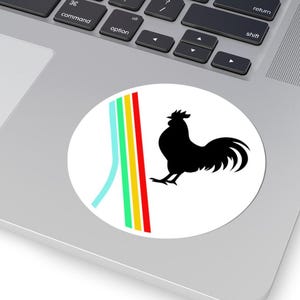 Può includere: Un adesivo rotondo con una silhouette di gallo nero su sfondo bianco. Il design include una striscia verticale blu, verde, gialla e rossa. L'adesivo è posizionato su un laptop.