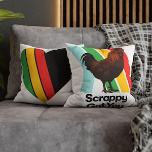 May include: Two white throw pillows with colorful designs. One features a heart shape with black, yellow, red, and green stripes. The other has a brown rooster on a striped background with the text "Scrappy Got You".