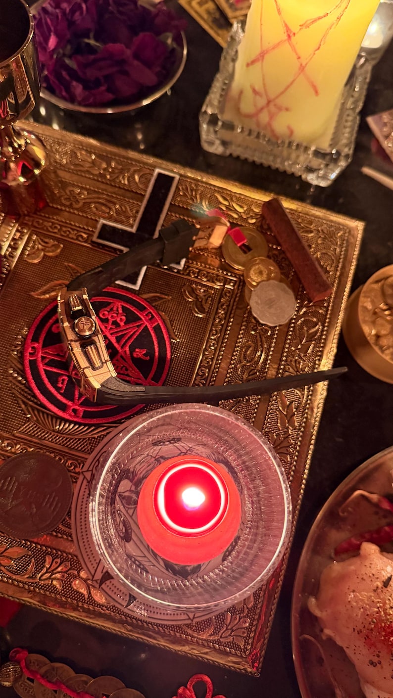 May include: A gold-toned wristwatch with a black rubber strap featuring a prominent crown and side detailing, resting on a rectangular gold-coloured metal plate engraved with a black cross and a red circular emblem with black symbols.