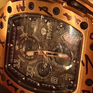 May include: A copper-toned tonneau-shaped wristwatch with a black dial featuring the text TSAR BOMBA. The bezel displays black engraved symbols, and the watch includes three sub-dials, luminous hands, and large Arabic numerals for the hours 1, 10, 11, and 12.
