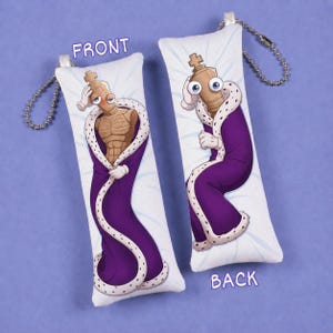 Könnte beinhalten: Zwei rechteckige Plüsch-Schlüsselanhänger mit einer Cartoon-Schachkönig-Figur mit großen Augen, die einen violetten königlichen Umhang mit weißem Pelzbesatz trägt. Die Figur hat einen beigen, muskulösen Oberkörper auf der Vorderseite und einen beigen Rücken.