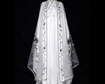 Könnte beinhalten: Weißes traditionelles chinesisches Hanfu-Kleid mit langem, fließendem Rock und einem transparenten Überzug. Der Überzug und die Verzierungen sind mit schwarzer Blumenstickerei verziert. Das Kleid wird auf einer Schaufensterpuppe vor schwarzem Hintergrund präsentiert.