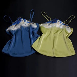 May include: Two silk camisoles, one in a deep blue and the other in a soft green. Both feature delicate embroidered detailing in white and blue along the neckline. The camisoles have thin spaghetti straps and a flowing, relaxed fit.