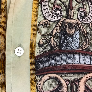 May include: A beige button-up shirt with a yellow and brown patterned design. The pattern features a stylized floral design with intricate details.