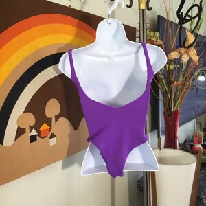 Pode incluir: Um mai&ocirc; roxo em um manequim branco. O mai&ocirc; tem um decote redondo e costas baixas.