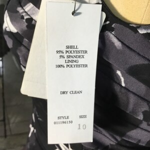 May include: A white tag with black text detailing the fabric composition and care instructions for a black and white patterned dress. The tag also includes the style number 011196150 and size 10.