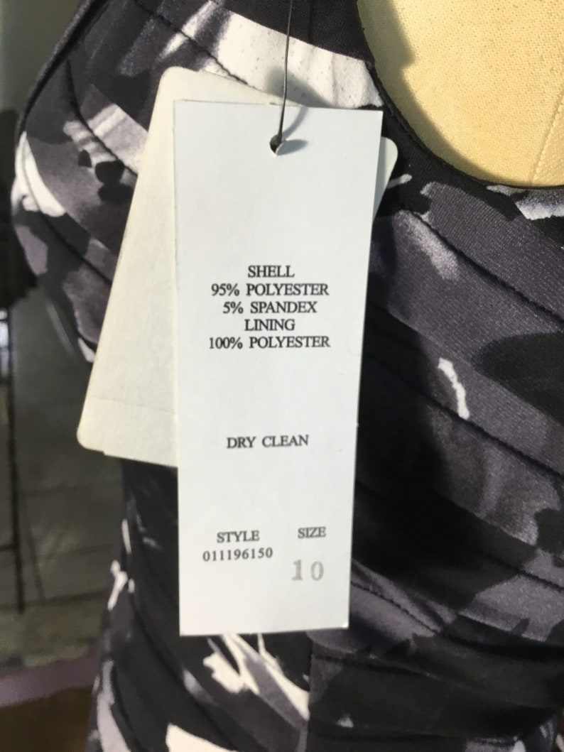 May include: A white tag with black text detailing the fabric composition and care instructions for a black and white patterned dress. The tag also includes the style number 011196150 and size 10.