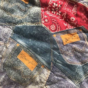 May include: A blue and red fabric with a patchwork design featuring denim pockets with the Wrangler logo. The fabric has a distressed look and is made of a soft, comfortable material.