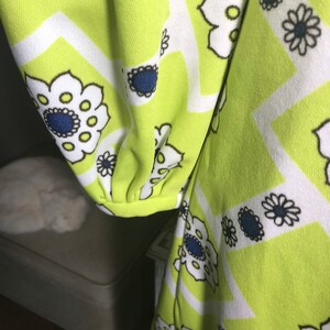 May include: A green fabric with a white and black geometric pattern featuring stylized flowers. The flowers have a blue center and white petals.