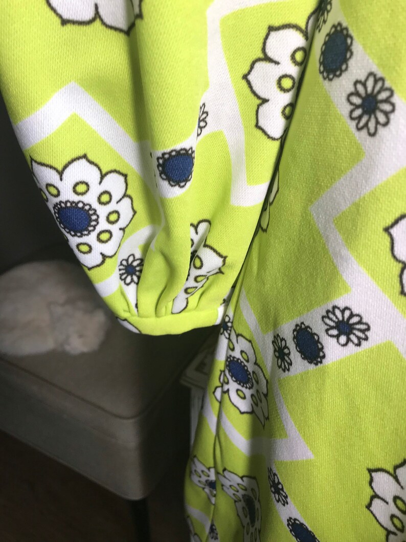 May include: A green fabric with a white and black geometric pattern featuring stylized flowers. The flowers have a blue center and white petals.