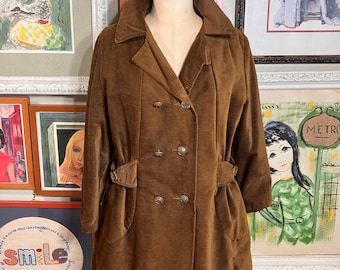 May include: A brown corduroy coat with a double breasted closure and a belt at the waist. The coat has two pockets on the front and is lined with a brown fabric.