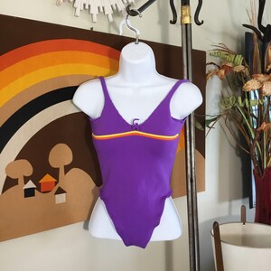 Pode incluir: Mai&ocirc; roxo com textura canelada e uma faixa amarela, laranja e vermelha no peito.