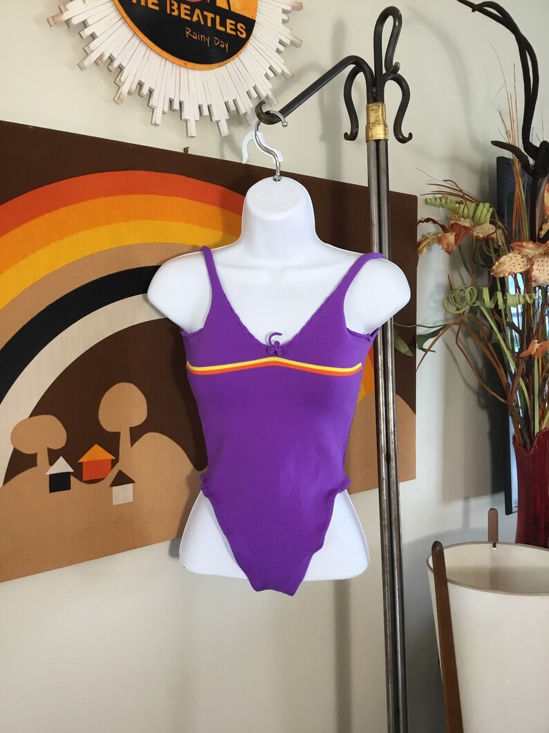 Pode incluir: Mai&ocirc; roxo com textura canelada e uma faixa amarela, laranja e vermelha no peito.