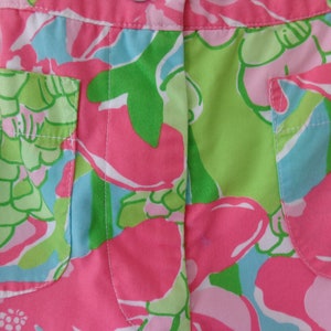 May include: Pink, green, and blue floral print fabric with two pockets. The fabric has a white stitching detail.