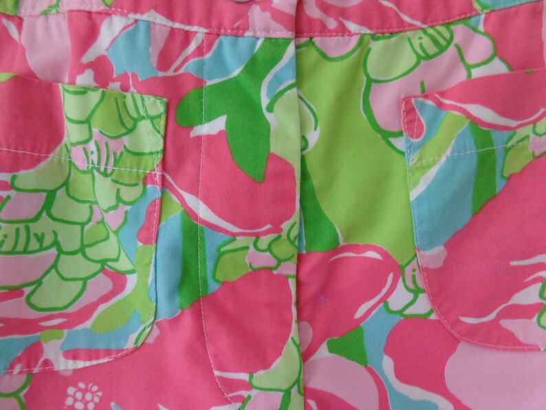 May include: Pink, green, and blue floral print fabric with two pockets. The fabric has a white stitching detail.