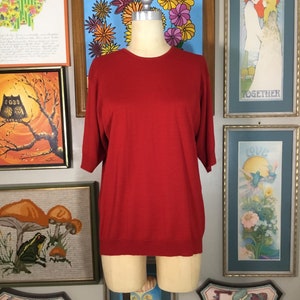 May include: A red, short-sleeved, crew neck sweater on a mannequin.