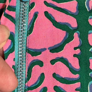 K&ouml;nnte beinhalten: Nahaufnahme eines t&uuml;rkisfarbenen Rei&szlig;verschlusses auf einem pink- und gr&uuml;n gemusterten Stoff.