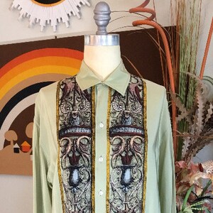 May include: A light green long-sleeved button-down shirt with a patterned design featuring intricate details in shades of brown, gold, and black.