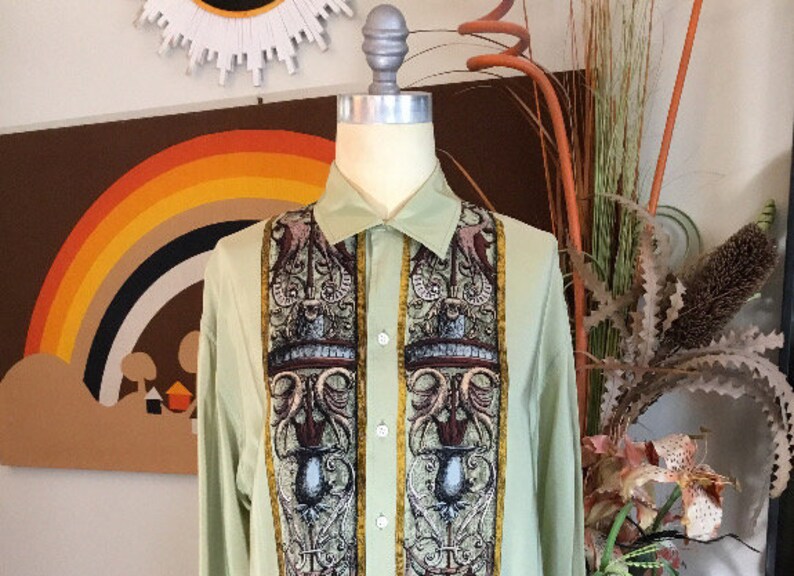 May include: A light green long-sleeved button-down shirt with a patterned design featuring intricate details in shades of brown, gold, and black.