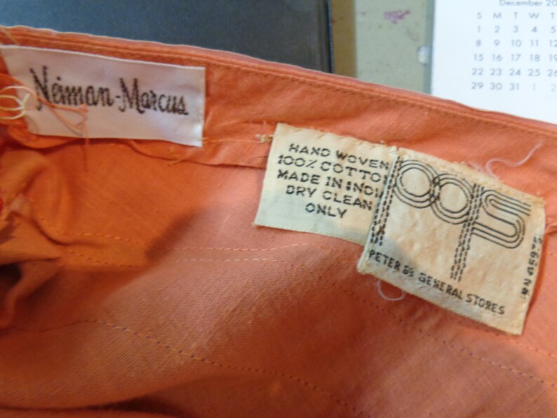 May include: A peach-colored garment with two white labels. The larger label reads "Neiman Marcus". The smaller label reads "Hand Woven 100% Cotton Made in India Dry Clean Only" and "Peter De General Stores".