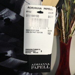 May include: A black and white dress with a printed pattern. The dress has a tag attached with the brand name "Adrianna Papell", style number "011196150", colour "BGY", description "CRS OV PNT TCK DS", and size "10".