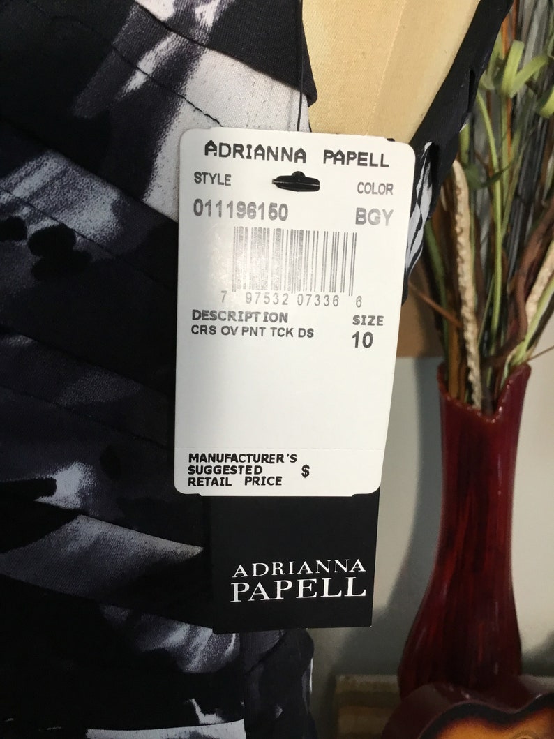 May include: A black and white dress with a printed pattern. The dress has a tag attached with the brand name "Adrianna Papell", style number "011196150", colour "BGY", description "CRS OV PNT TCK DS", and size "10".