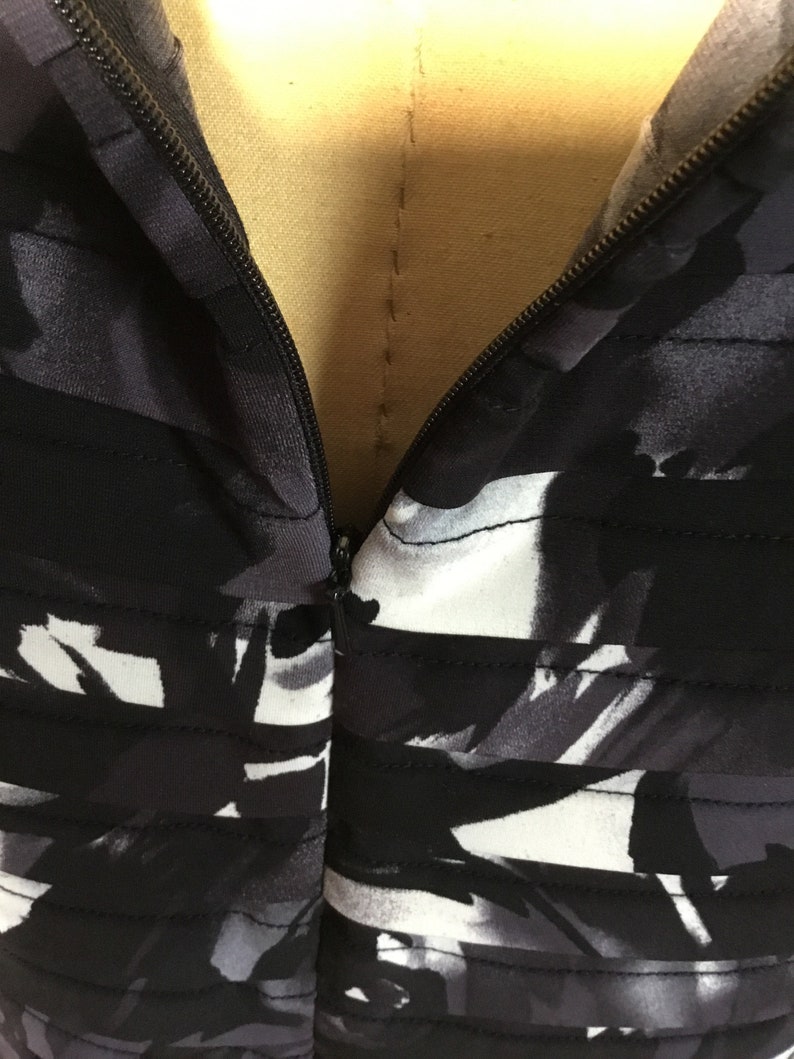 May include: Black and white abstract print dress with a zip closure at the front.