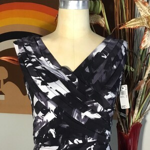 May include: A black and white sleeveless dress with a V-neckline and a pleated design. The dress has an abstract print and a fitted silhouette.