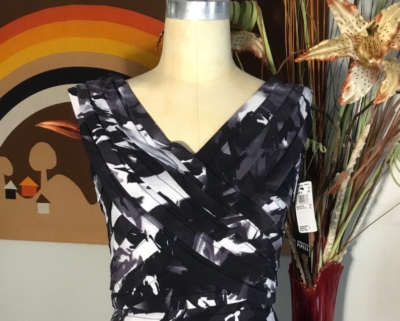 May include: A black and white sleeveless dress with a V-neckline and a pleated design. The dress has an abstract print and a fitted silhouette.