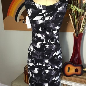 May include: A black and white patterned sleeveless dress with a scoop neck. The dress is on a white mannequin and has a fitted silhouette.
