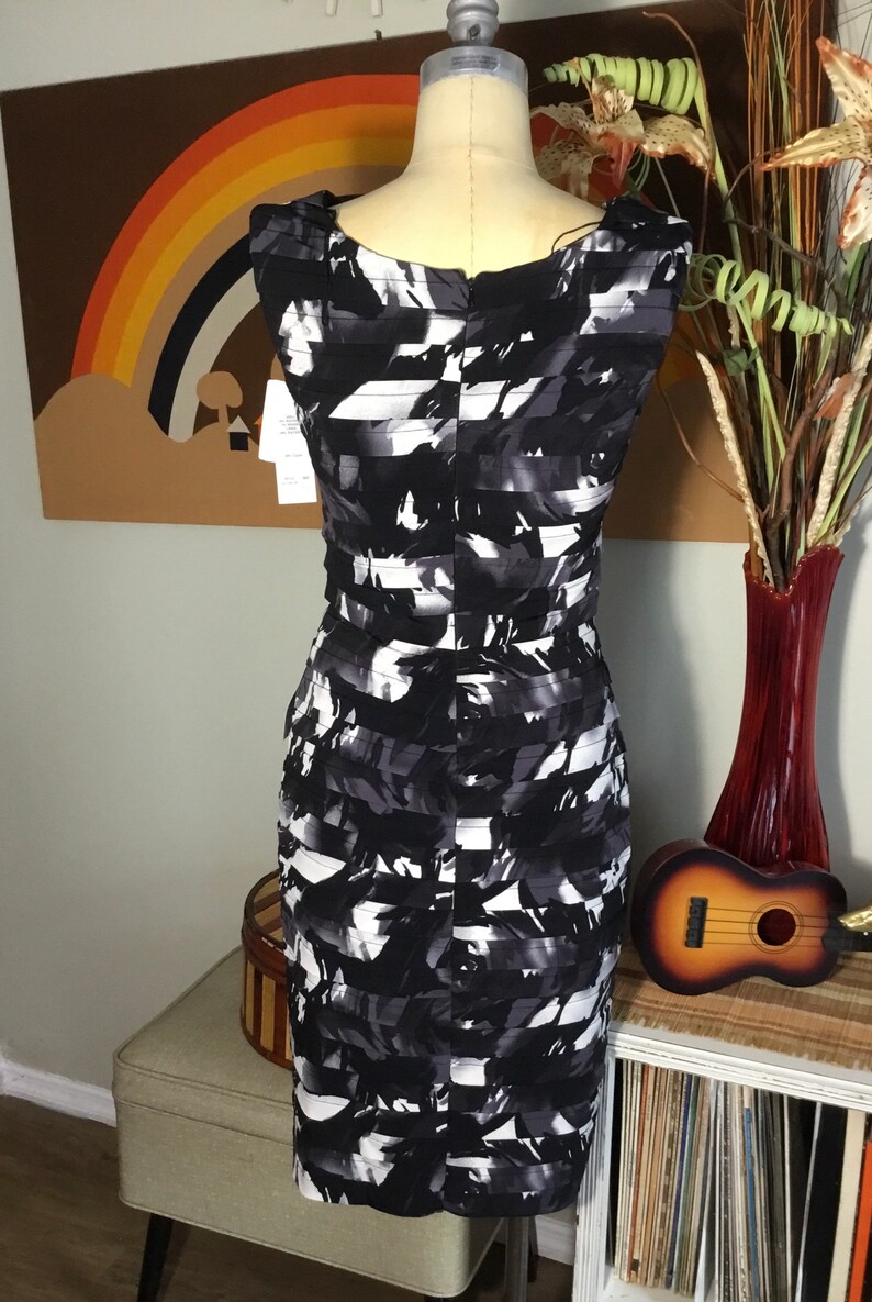 May include: A black and white patterned sleeveless dress with a scoop neck. The dress is on a white mannequin and has a fitted silhouette.
